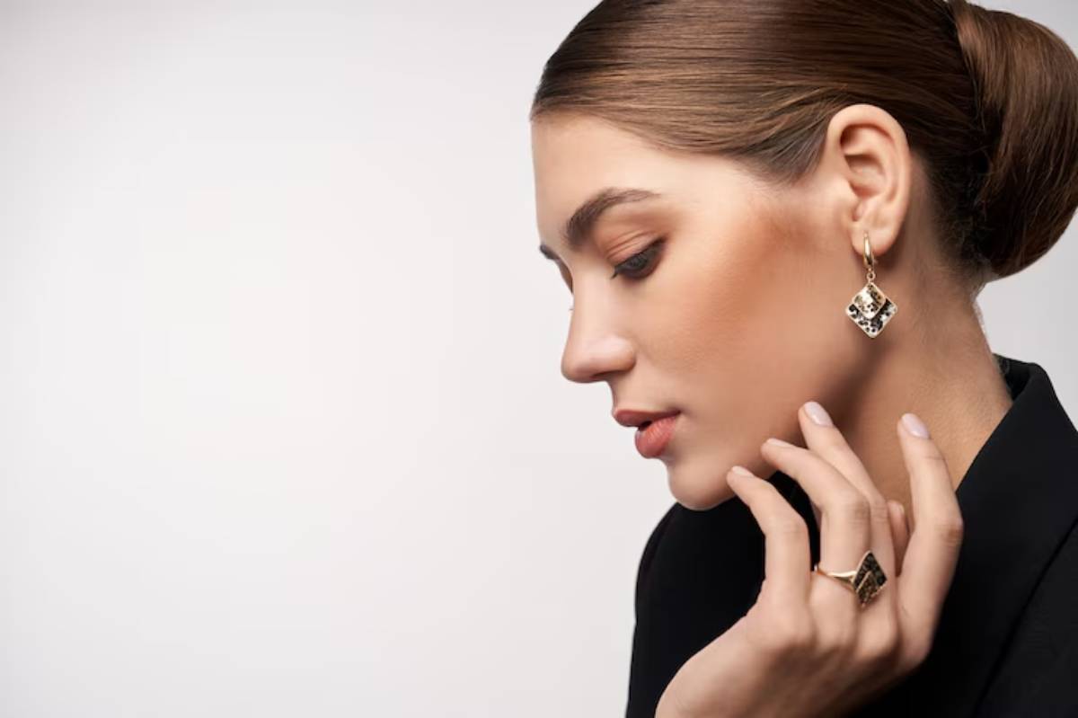 A close-up of a woman wearing stylish, geometric gold earrings and rings, showcasing elegant fashion against a minimalist background.