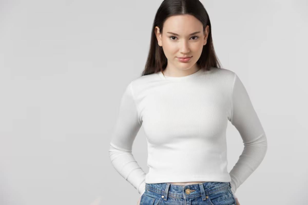 A woman in a white long-sleeve base top stands confidently against a neutral background.