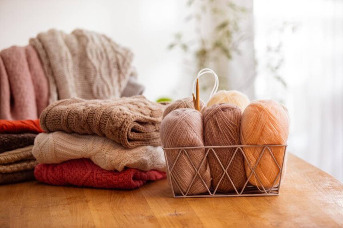 A cozy arrangement of knitted sweaters beside a basket of yarn in warm tones.