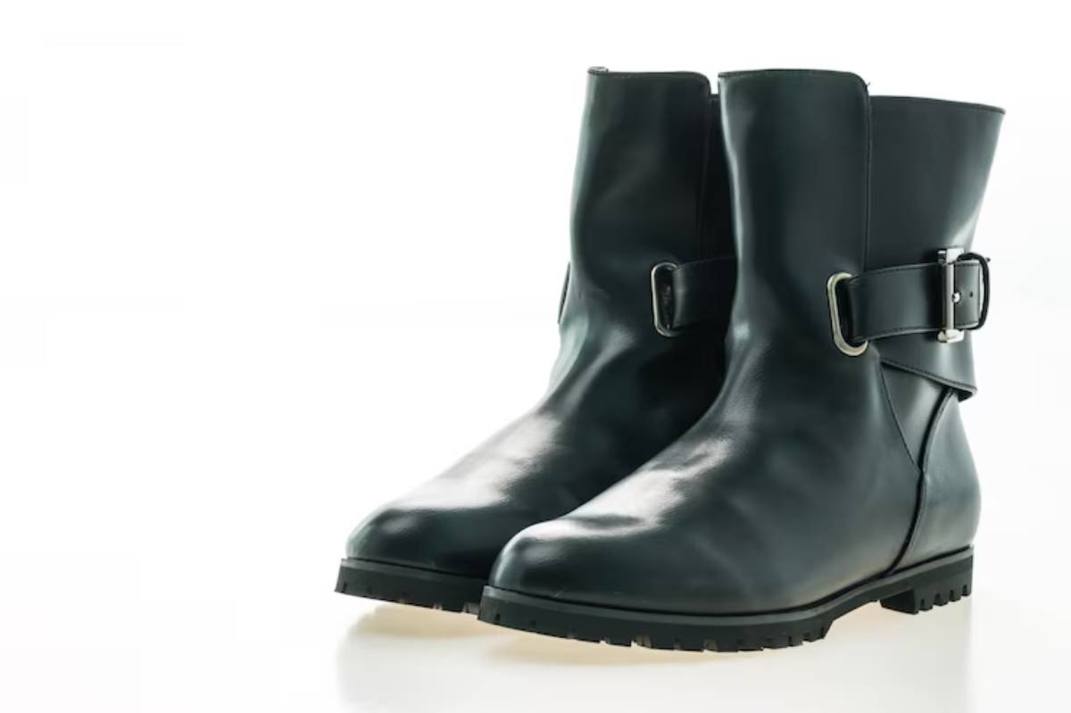 Pair of sleek black leather ankle boots with a side buckle and rugged sole, set against a bright, minimalist background.