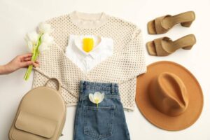 A stylish outfit layout featuring a knit sweater, white shirt, denim shorts, heels, a hat, and tulips for a fresh look.