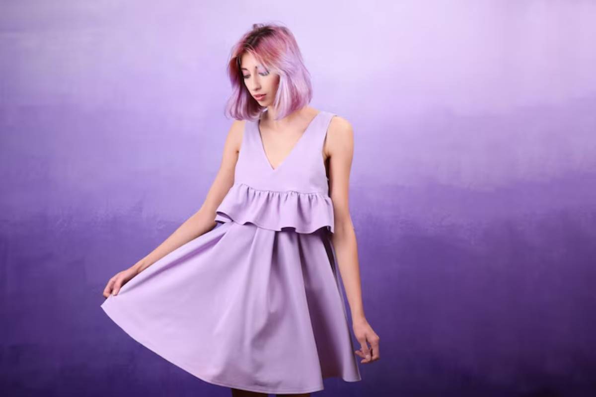 A fair skin model poses confidently in a lavender dress with a ruffled hem against a soft purple background, showcasing a chic, playful style.