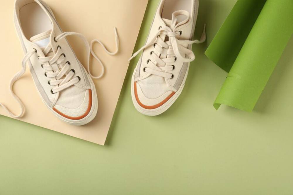A pair of beige sneakers with orange accents on a pastel backdrop, surrounded by green and beige paper rolls.
