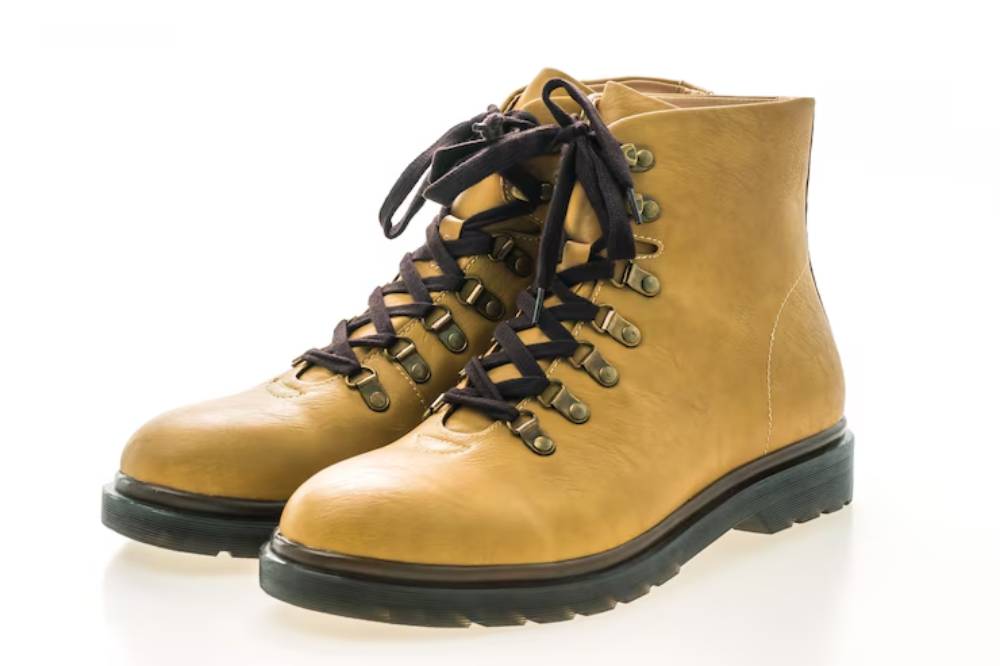 A pair of tan leather hiking boots with dark laces, set against a bright background, showcasing their rugged design and sturdy soles.