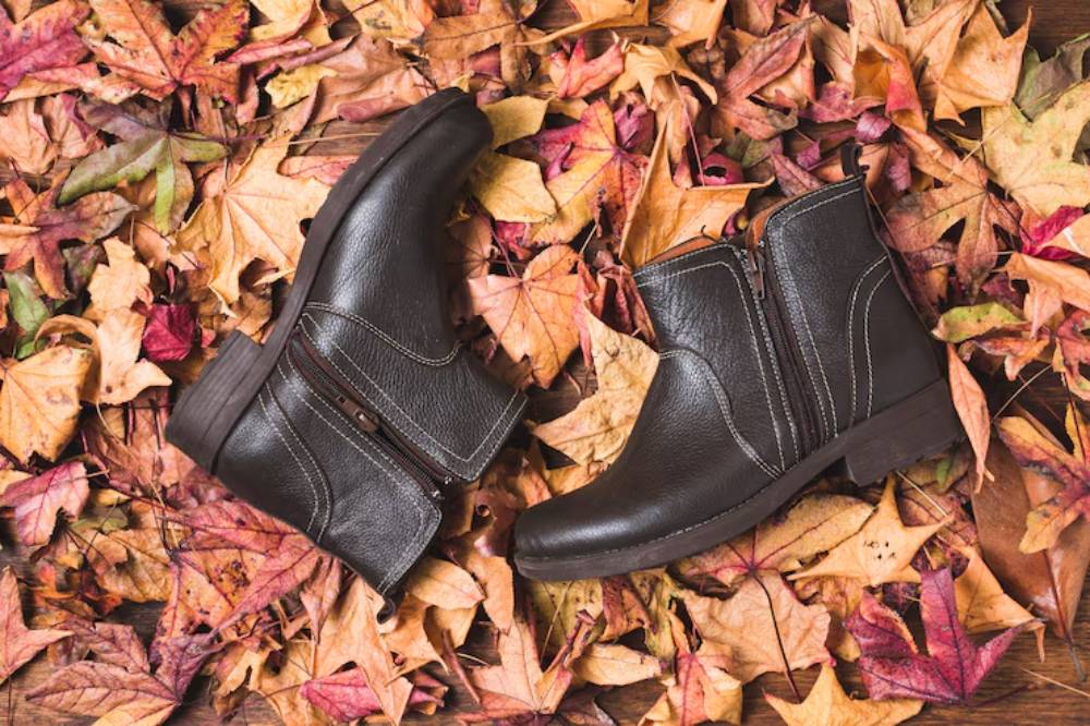 Stylish black leather boots resting on a bed of colorful autumn leaves, highlighting seasonal fashion and nature's beauty.