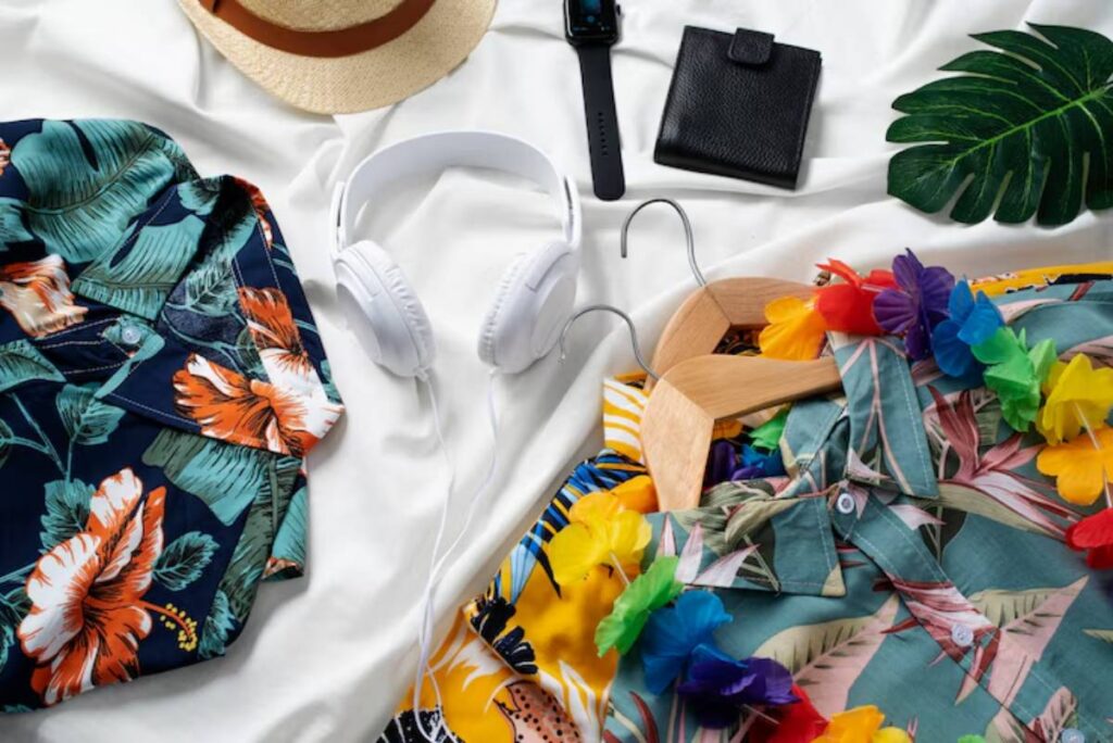 Colorful tropical shirts, a straw hat, headphones, a watch, and a wallet arranged on a white background, with floral accessories.