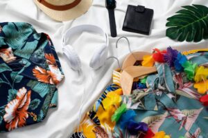 Colorful tropical shirts, a straw hat, headphones, a watch, and a wallet arranged on a white background, with floral accessories.