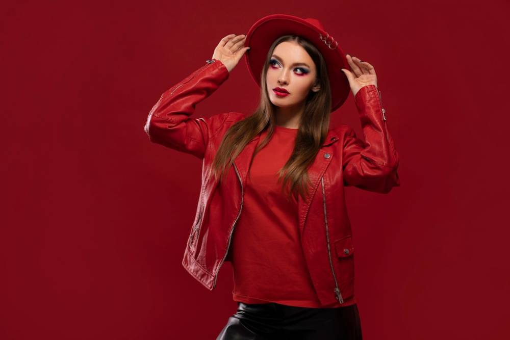 A person in ruby red leather jacket and matching hat poses confidently against a solid red background.