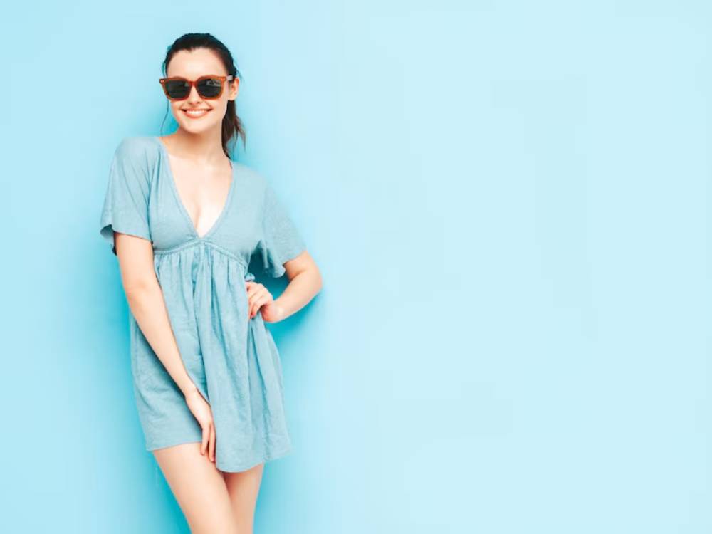 A person poses confidently in a loose-fitting, sky blue dress against a solid pastel blue background.