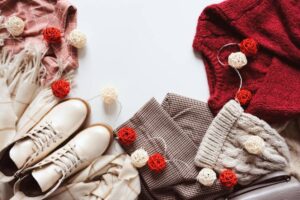 A cozy flat lay featuring a maroon sweater, beige scarf, checked pants, white boots, and colorful decorative lights.